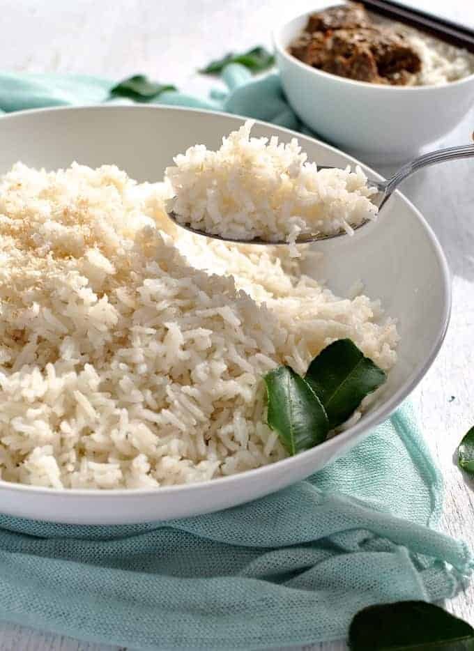 A spoon scooping up some fluffy coconut rice in a white bowl.