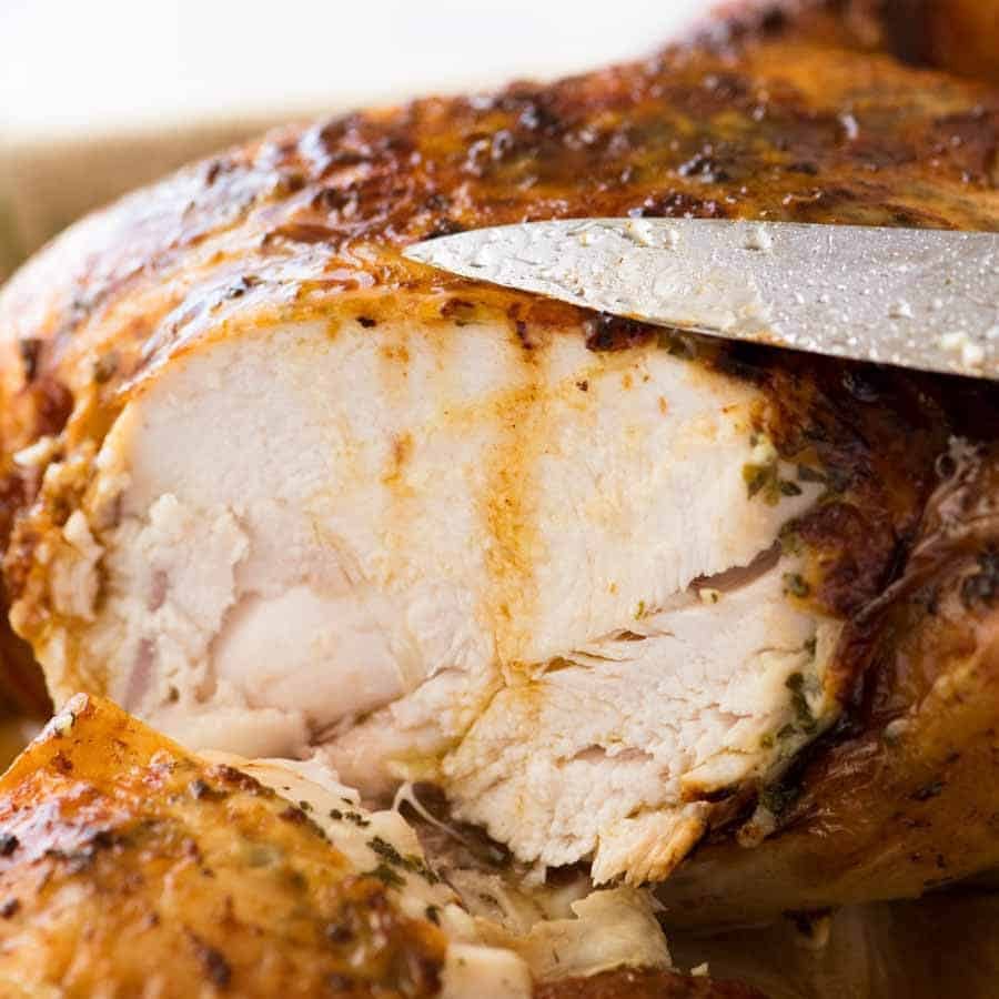 Close up of cut crispy skin Roast Chicken with garlic herb lemon butter juices running down the side.