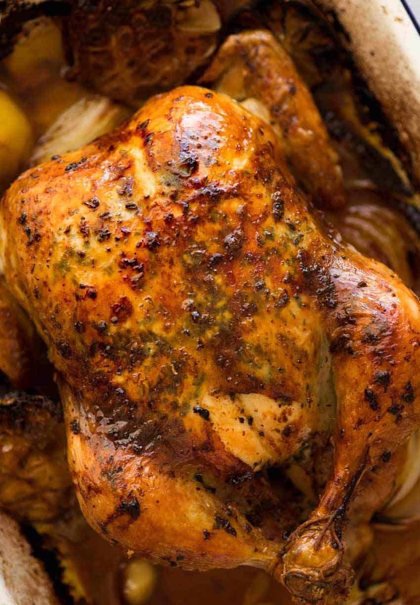 Overhead photo of golden Roast Chicken with crispy skin, fresh out of the oven, bathed in garlic-herb-lemon butter.