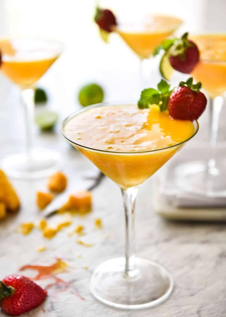 Mango Daiquiris in cocktail glasses garnished with strawberries.