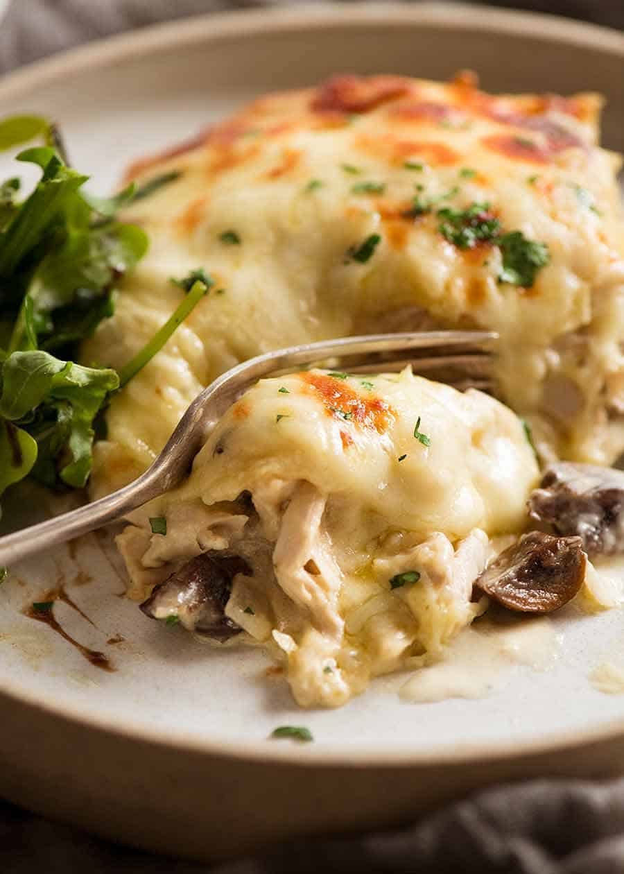 Close up of fork cutting into slice of Chicken Lasagna on a plate, ready to be eaten