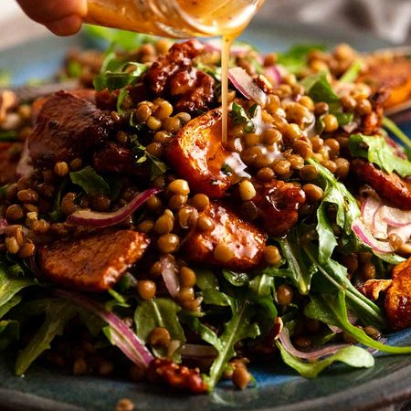 Pouring dressing over Honey Cinnamon Pumpkin Lentil Salad